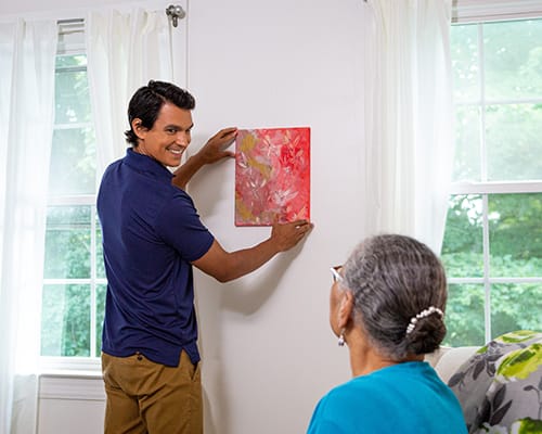 caregiver hanging a painting for a resident