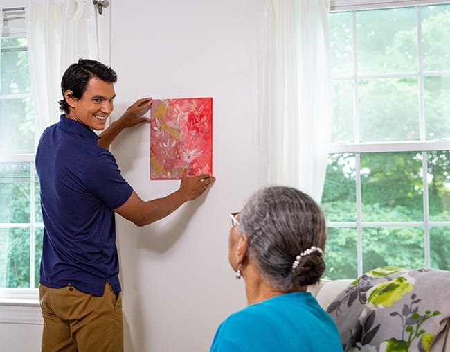 caregiver helping resident hang a painting
