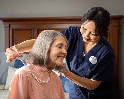 caregiver helping resident put on a necklace
